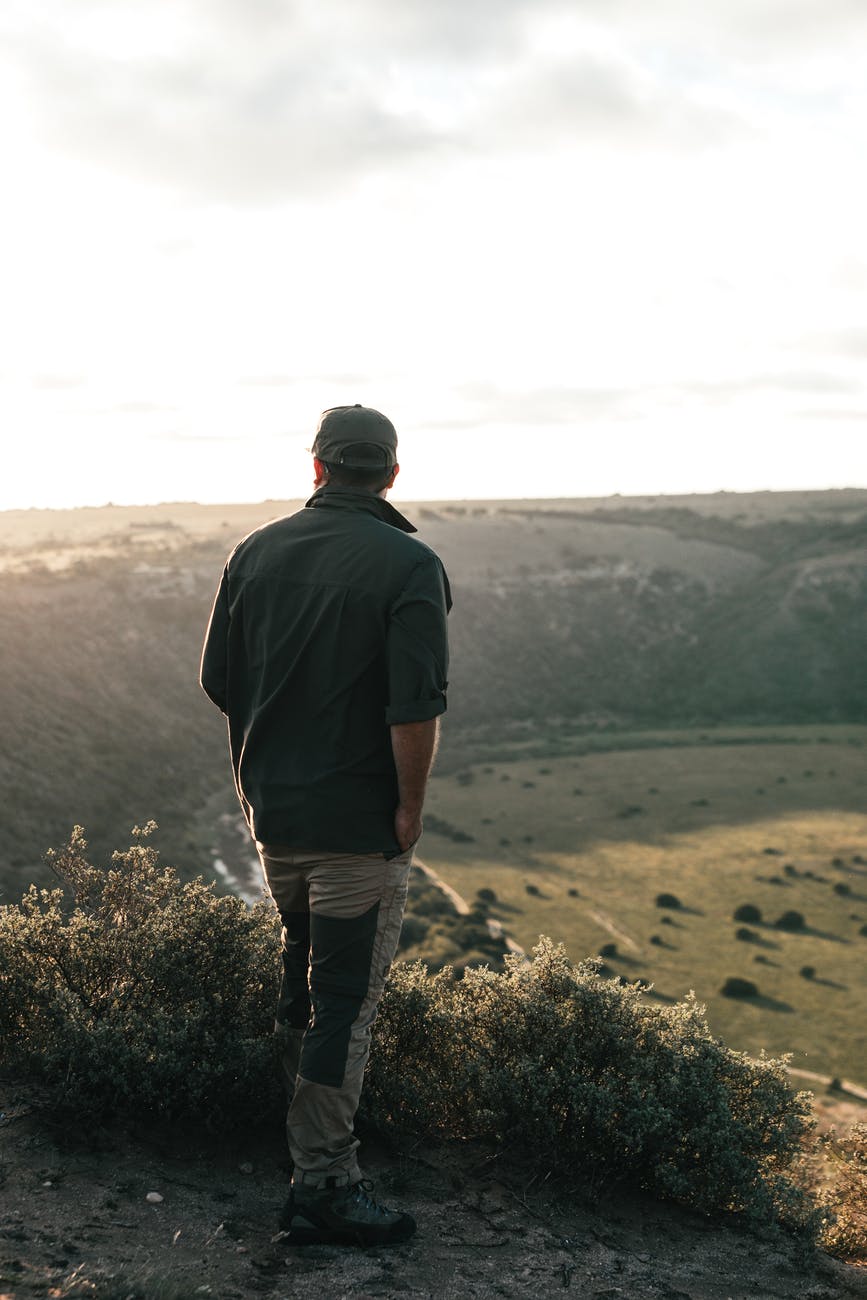 unrecognizable traveler contemplating green mountain in sunlight